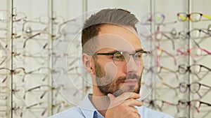 Confused man chooses glasses at optical shop