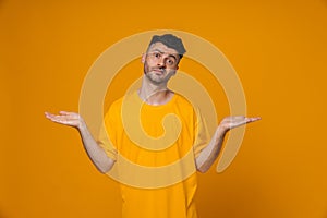 Confused man holding copyspace on two palms isolated over yellow wall