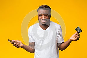 Confused Man Holding Phone And Credit Card Over Yellow Background