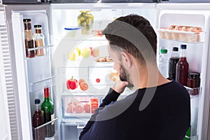 Confused Man Looking At Food In Refrigerator