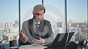 Confused man reading sms checking smartphone. Unhappy manager work typing laptop