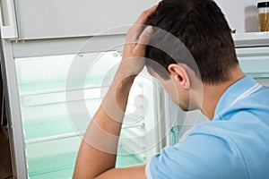Confused Man Scratching Head While Looking At Empty Refrigerator