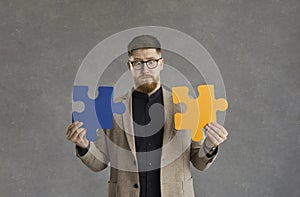 Confused man trying to connect two jigsaw puzzle pieces as metaphor for problem solving