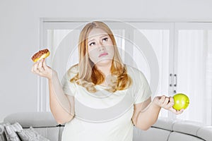 Confused obese woman with donuts and apple fruit