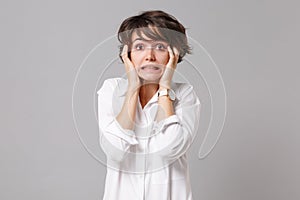 Confused puzzled young business woman in white shirt posing isolated on grey wall background studio portrait