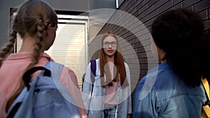 Confused red-haired teenager in eyeglasses standing front of cruel classmates