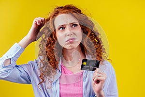 Confused redhaired ginger curly woman colding plastic creditcard and looking upsad .rejection concept