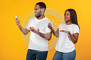 Confused sad millennial african american couple looking at their phones