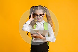 Confused Schoolgirl Using Digital Tablet On Yellow Background