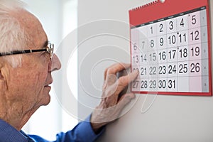 Confused Senior Man With Dementia Looking At Wall Calendar