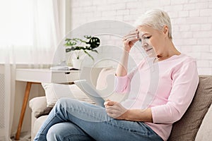 Confused senior woman using tablet computer at home