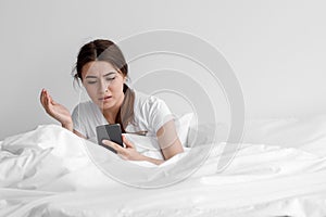 Confused shocked upset european young female received bad message, sits on white bed in bedroom interior