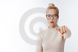 Confused and shocked woman seeing celebrity standing in stupor and frustration pointing at camera dropping jaw looking photo
