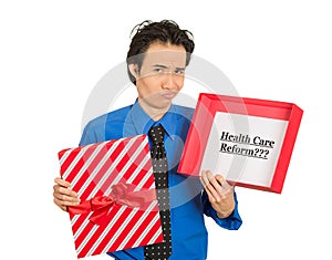 Confused skeptical man holding sign health care reform in gift box