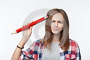 Confused teen girl student scratching her head with big pencil