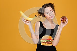 Confused thoughtful young woman choosing between healthy and unhealthy food