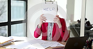 Confused tired woman sitting in office holds inscription help
