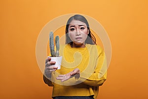 Confused uncertain asian woman gesturing unsurely while holding cactus plant.