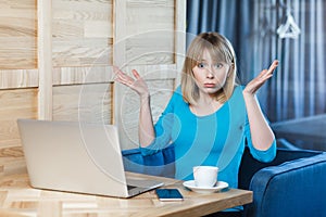 Confused uncertain woman working on laptop, shrugging shoulders, looking at camera with puzzled face
