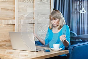 Confused uncertain young woman working on laptop, shrugging shoulders, looks doubtful and puzzled.