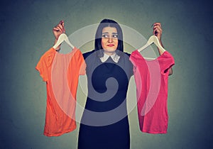 Confused woman choosing between dresses and can not make decision.