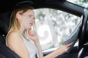 confused woman in drivers seat car looking at map