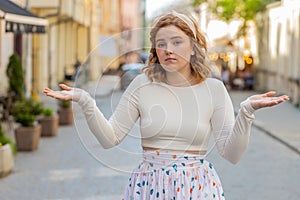 Confused woman feeling embarrassed about ambiguous question having doubts no idea in city street photo