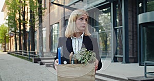 Confused woman in formal suit holding box with her stuff and looking aside. Embarassed female worker making deep breath