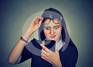Confused woman with glasses having trouble seeing cell phone photo