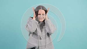 Confused woman holding hands on ears and shouts over turquoise studio background