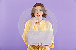 Confused woman isolated over purple wall background using laptop computer.