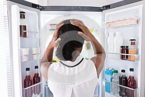 Confused Woman Looking In Open Refrigerator