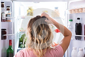 Confused Woman Looking In Open Refrigerator