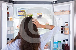 Confused Woman Looking In Open Refrigerator