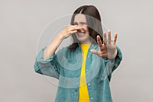 Confused woman pinching nose to hold breath and showing stop gesture disgusted by unpleasant odor.