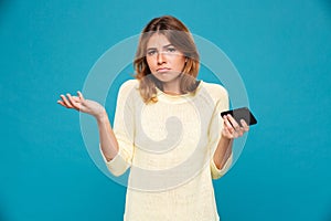 Confused woman in sweater holding smartphone and shrugs her shoulder