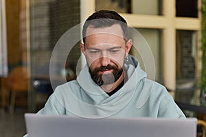 Confused young adult man in casual clothes in cafe using his laptop. Online business