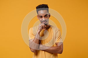 Confused young african american guy in casual t-shirt posing isolated on yellow orange wall background studio portrait