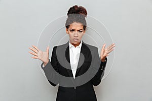 Confused young african business woman standing over grey wall