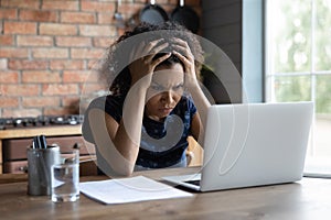 Confused young african ethnicity woman looking at computer screen.