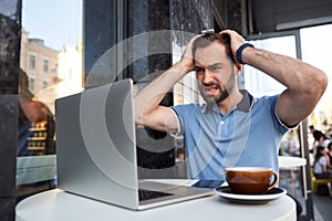 Angry bearded man with laptop in street cafe