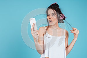 Confused young lady with hair curlers using phone