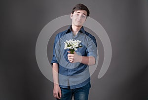 Confused young man in blue shirt holding in bouquet with snowdrops, looking at camera