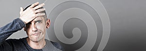 Confused young man holding his head, having regret, grey banner