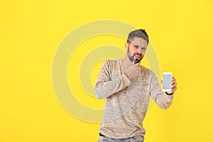 Confused young man with inoperable mobile phone on color background