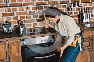 confused young repairwoman looking at broken oven