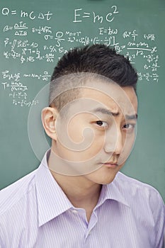 Confused young student in front of blackboard with math equations, making a face, portrait