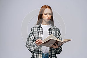 Confused young woman college student turning pages of book on gray isolated background.