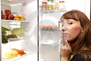 Confused young woman looking in fridge