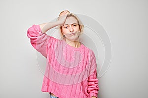 Confused young woman in pink sweater scratching head against grey background expressing uncertainty